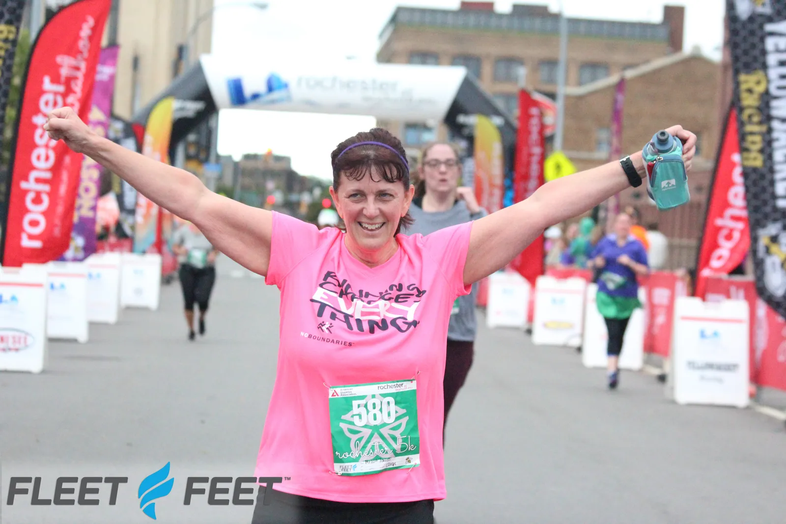 A female runner with her arms raised in celebration crosses the finish line, smiling broadly.
