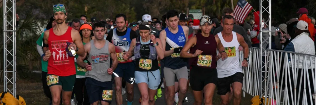 A group of runners at the start line of a race, with some spectators in the background.