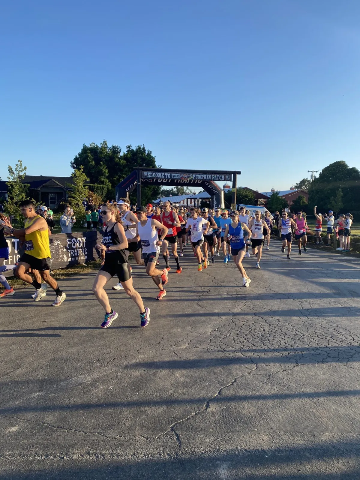 Runners starting a race under an archway that says 'Welcome to the Pumpkin Patch Foot Traffic'.
