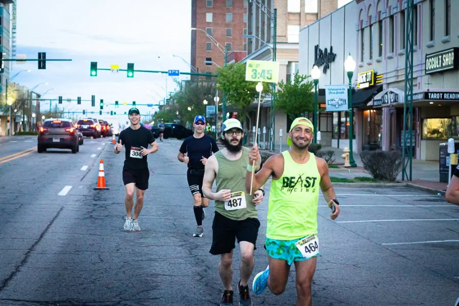 Runners on an urban street during a race, with buildings and traffic lights in the background.