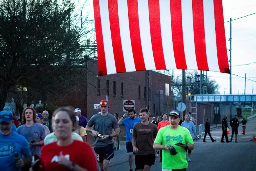 Runners participating in a race, with a large American flag hanging overhead.
