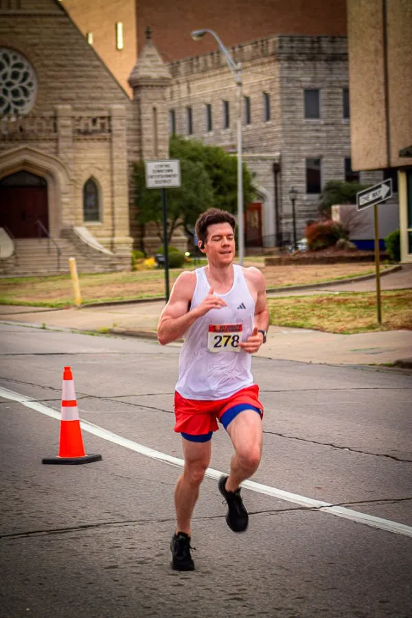 A male runner with bib number 278 runs on a road with buildings in the background.