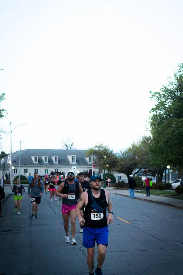 Runners on a road during a race, with a building and trees in the background.