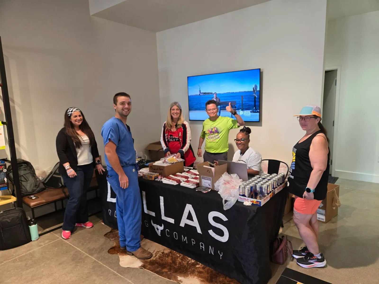 A group of people standing behind a table with race materials and drinks, smiling at the camera.