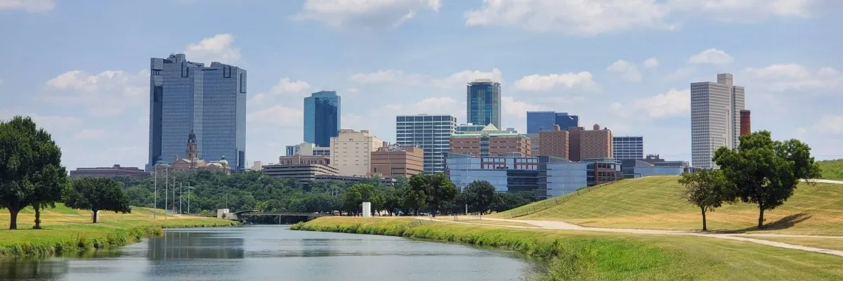 Scenic view of the Fort Worth skyline with a river in the foreground and grassy banks.