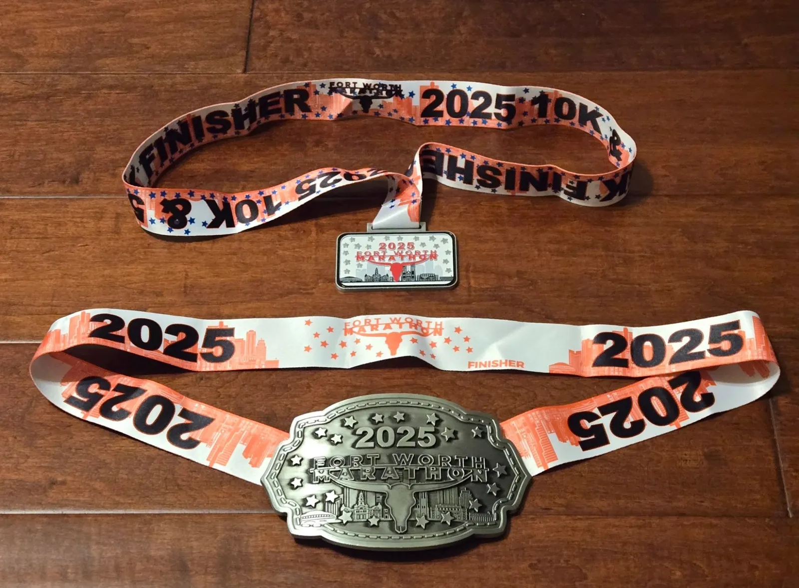 Two Fort Worth Marathon medals from 2025, one for the 10k and one for the marathon, displayed on a wooden surface.