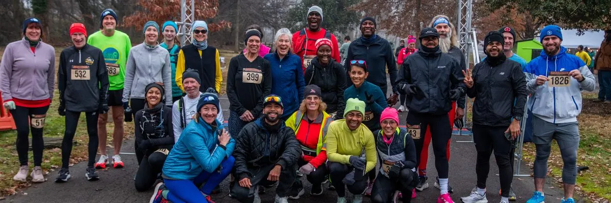A diverse group of runners, many smiling and wearing race bibs, pose for a photo before or after a race.