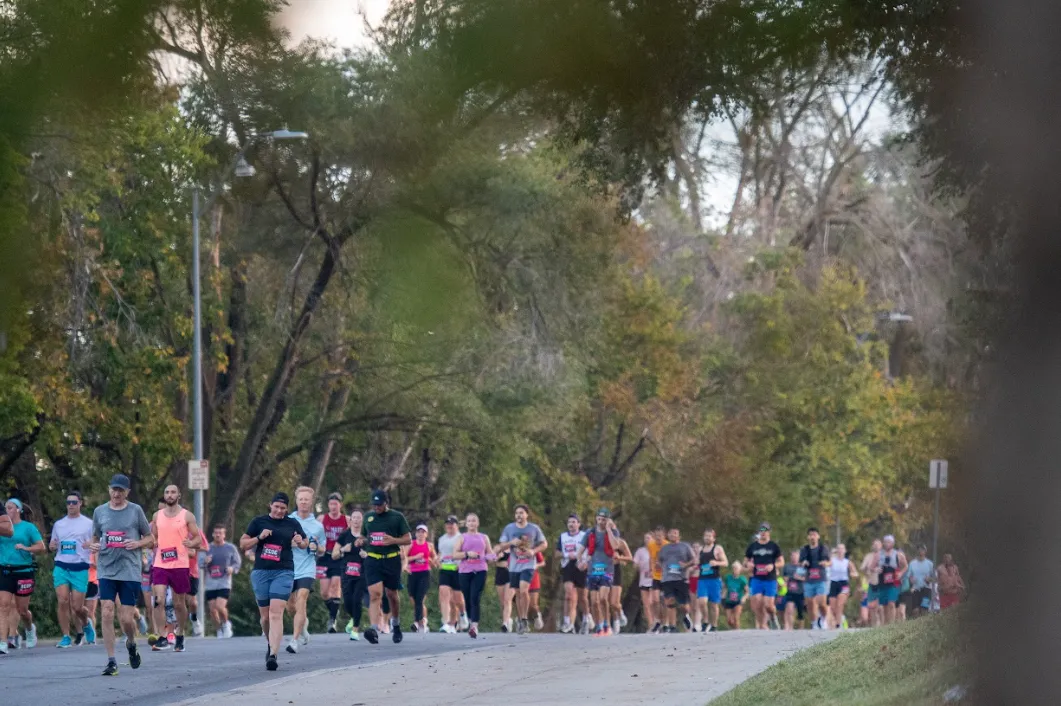 A group of runners participating in a road race, with trees and foliage in the background.