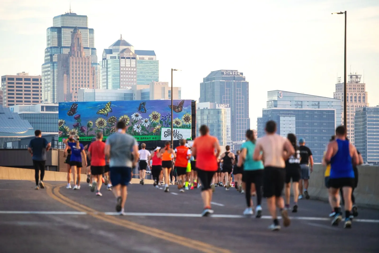 Runners on a road with a cityscape and a mural in the background.