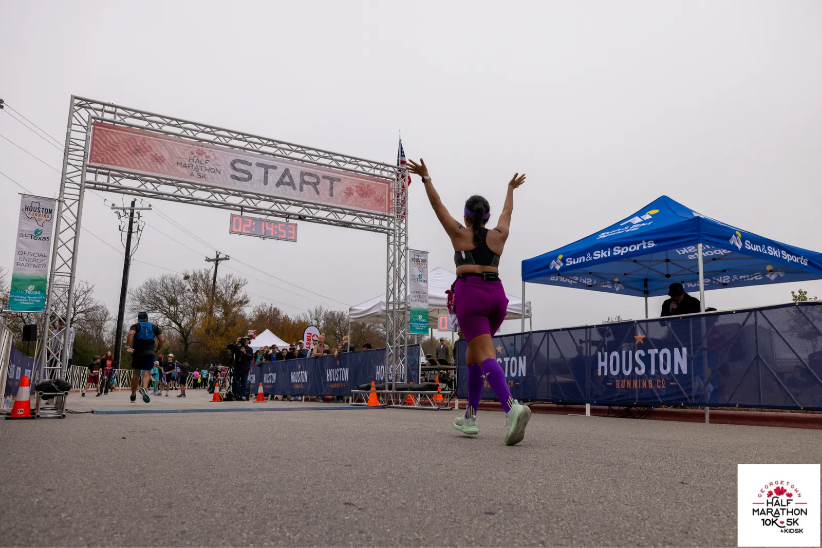 A female runner with arms raised in celebration crosses the start line of the Georgetown Half Marathon.