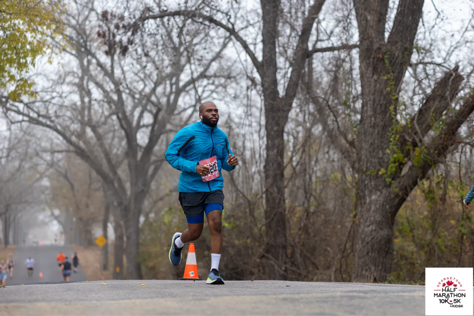 A male runner in a blue jacket runs on a road during the Georgetown Half Marathon.