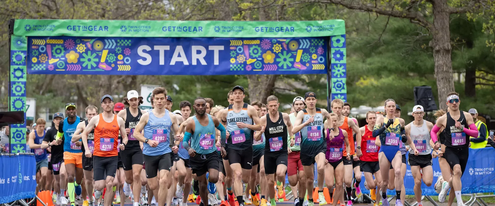 A large group of runners are starting a race under a colorful banner that says 'START'.