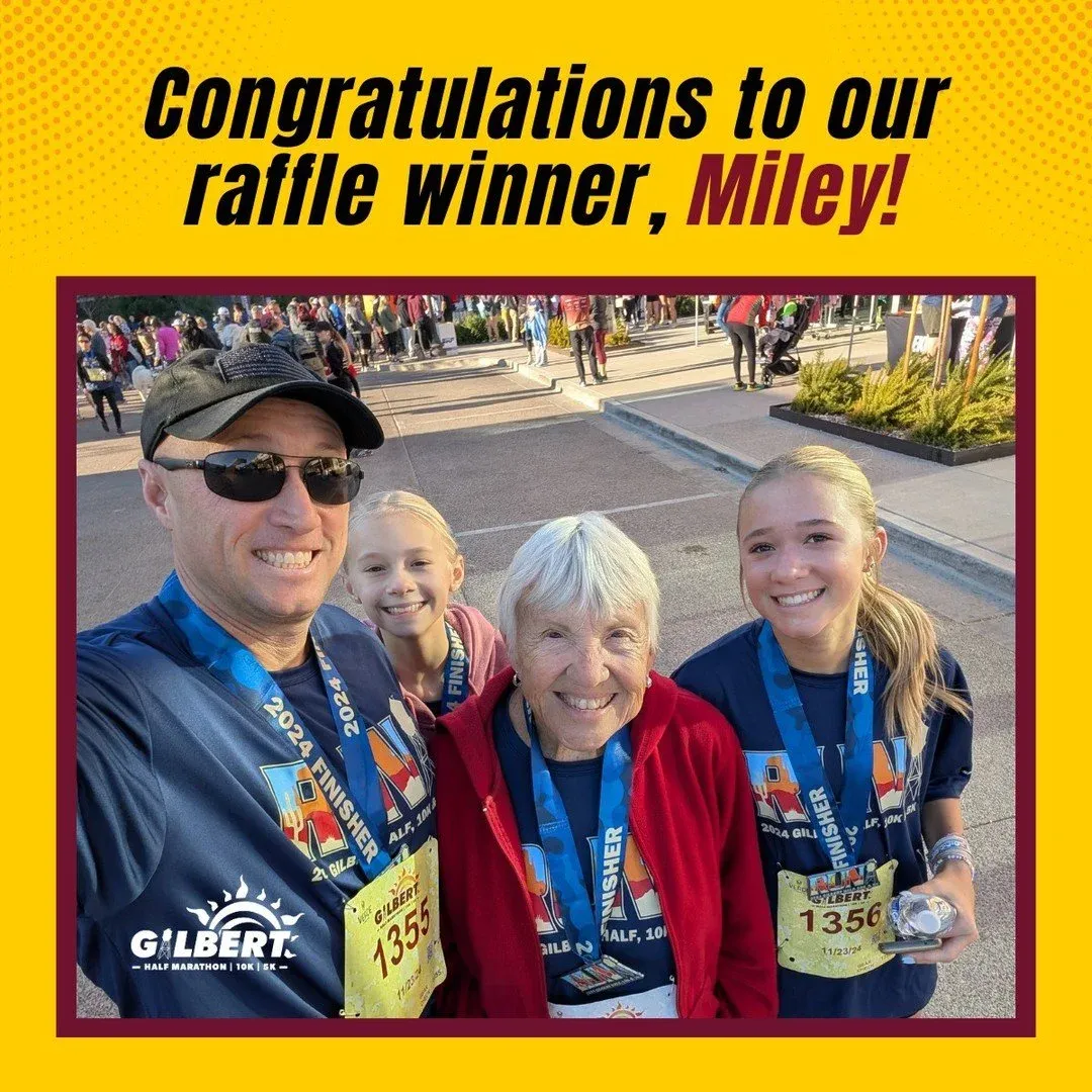 A group of four people, including a man, two young girls, and an older woman, smiling and wearing race medals and bibs from the Gilbert Half Marathon.
