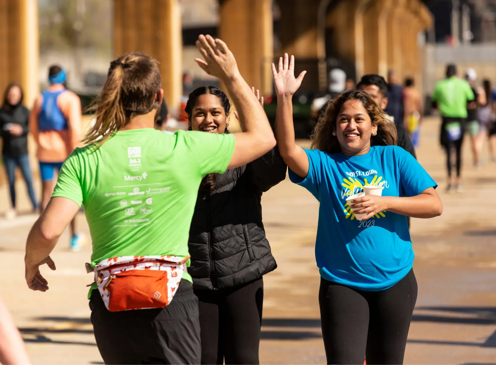 Three runners high-fiving each other during a race, with smiles and positive energy.
