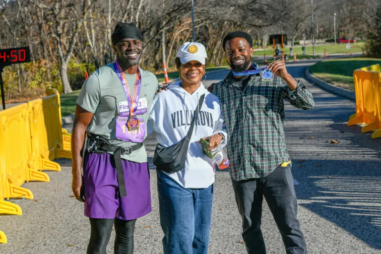 Three people smiling, two of them wearing race medals, with a timer showing 4:50 in the background.