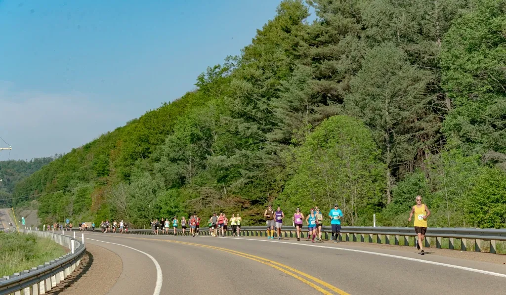 Runners on a road with a tree-covered hill in the background.