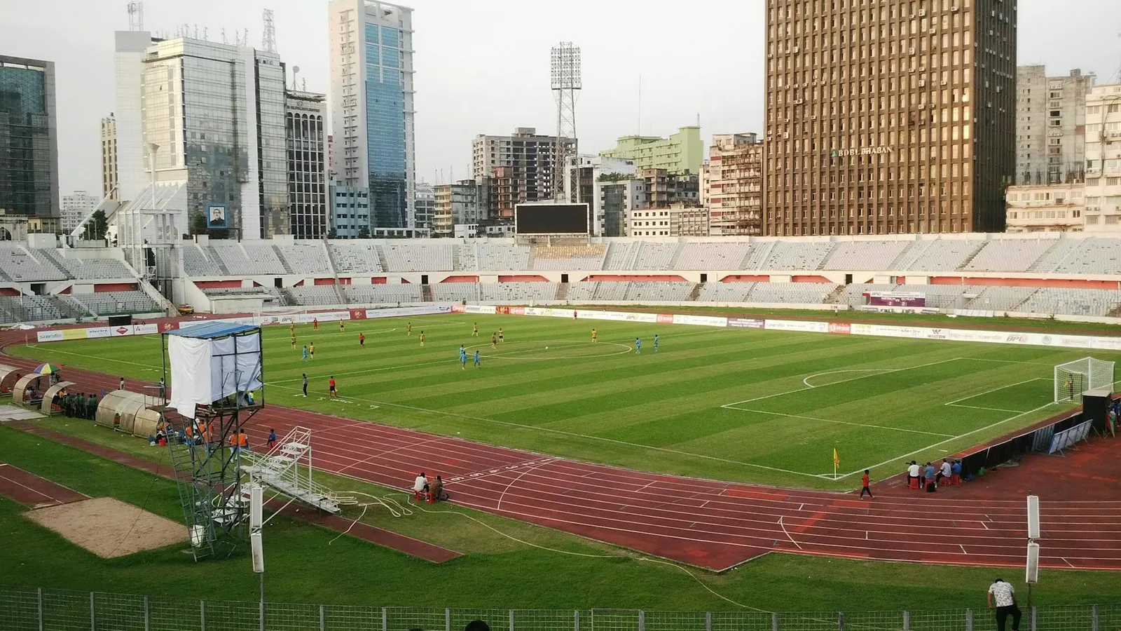 A stadium with a running track and a soccer field, with buildings in the background.
