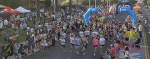 A large group of runners starting a race under blue inflatable arches, with spectators lining the street.