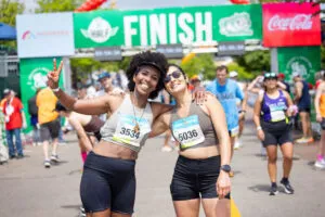 Two smiling women, one giving a peace sign, pose for a photo at the finish line of a race.