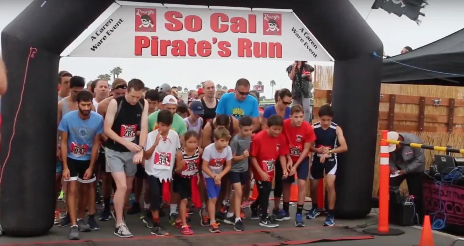 Runners of all ages lined up at the start of the So Cal Pirate's Run, under a large inflatable archway with the race name prominently displayed.