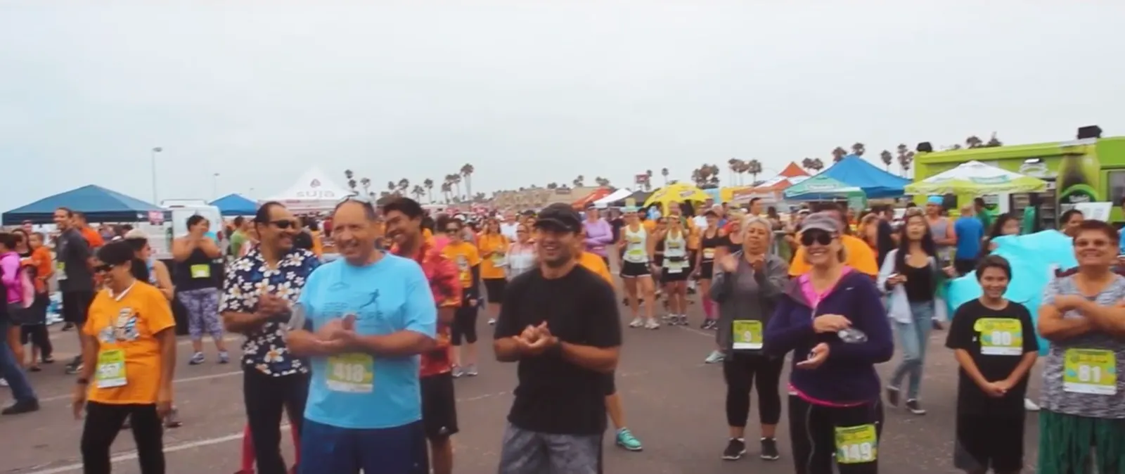 A crowd of people, some wearing race bibs, gathered at an outdoor event, possibly a race start line.