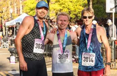 Three male runners smiling and posing for a photo, wearing race bibs and medals.