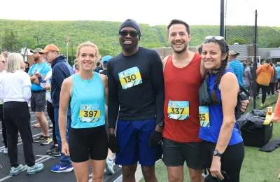 Four runners smiling at the camera, two women and two men, with race bibs visible.