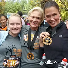 Three women smiling and holding up race medals after completing the Halloween Half Marathon.