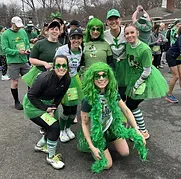 A group of runners dressed in green costumes and wigs pose for a photo at a race.