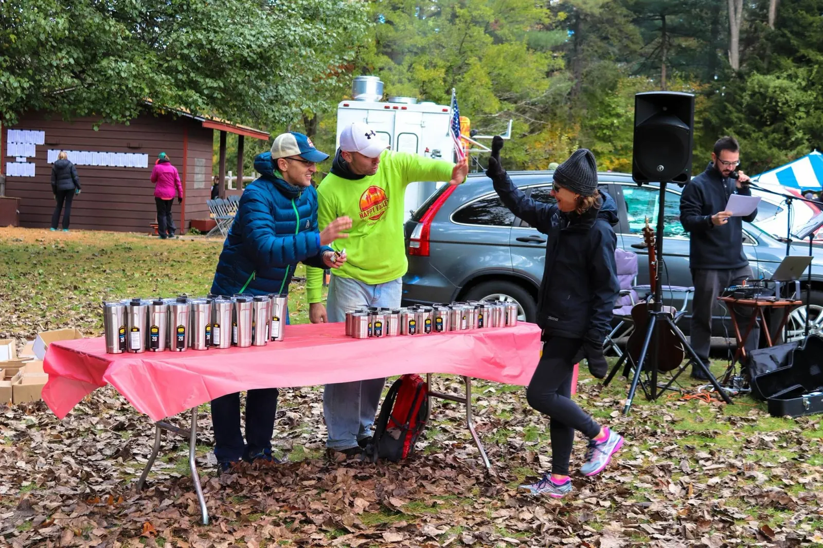 People gathered around a table with cups at a race event, with a person in a bright green shirt giving a high-five.