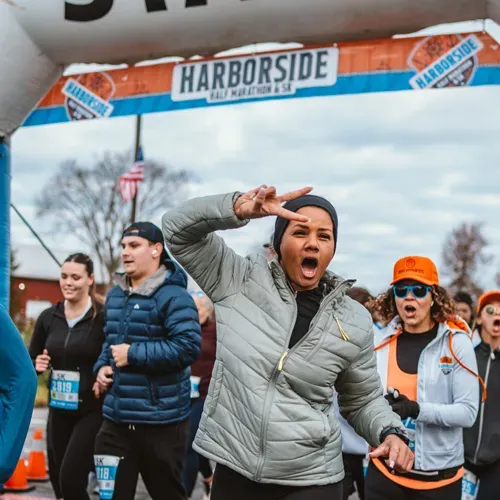 A runner at the start line of the Harborside Half Marathon & 5K makes a peace sign with a look of excitement.