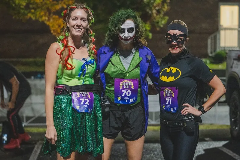 Three runners in costumes, including Poison Ivy, Joker, and Batman, posing at a race.