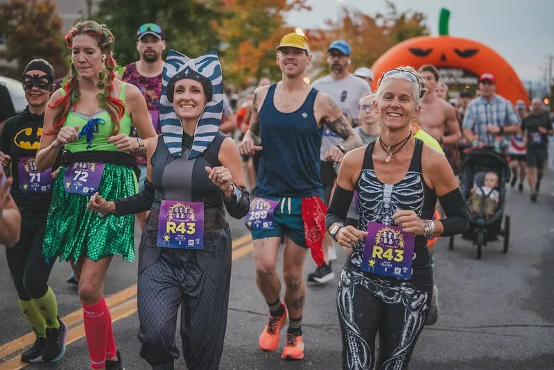 Runners in Halloween costumes participating in the Haunted Half Marathon, with a large inflatable pumpkin arch in the background.