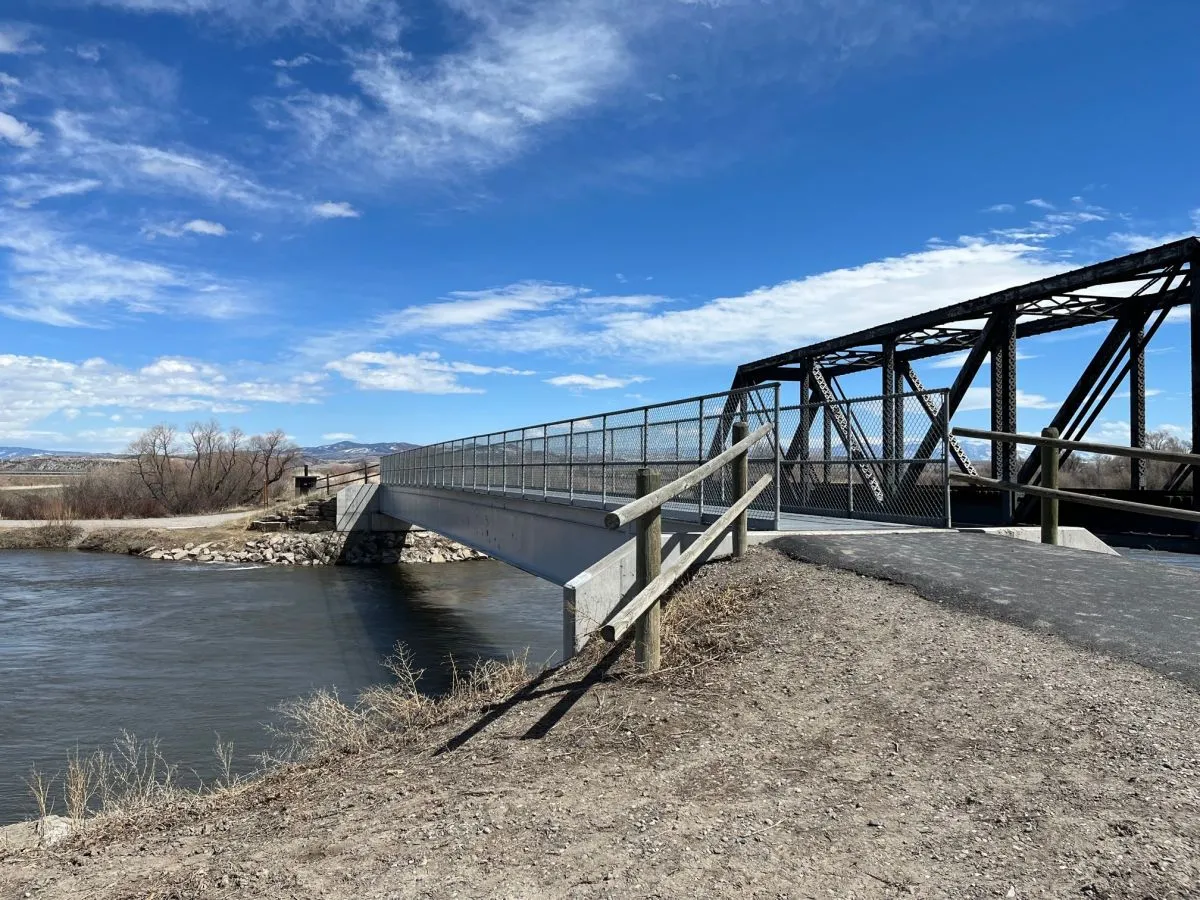 A bridge spans a river under a blue sky with scattered clouds.