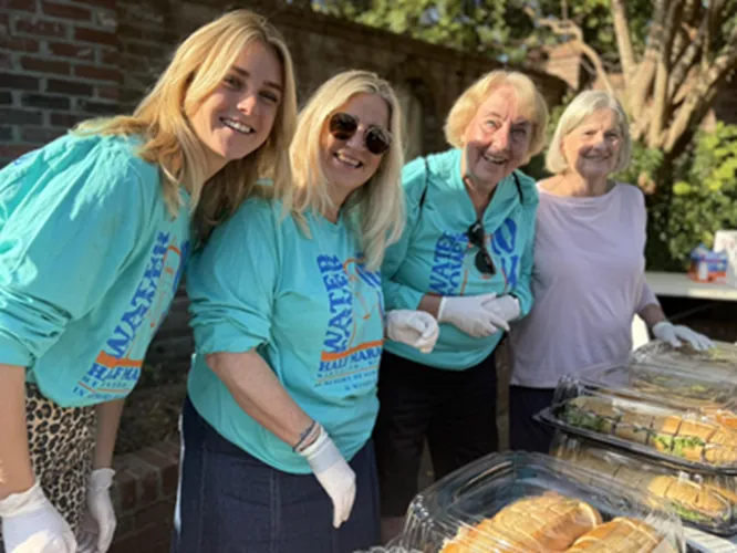 Four smiling people, some wearing race t-shirts, stand behind a table with food, possibly volunteers at a race event.
