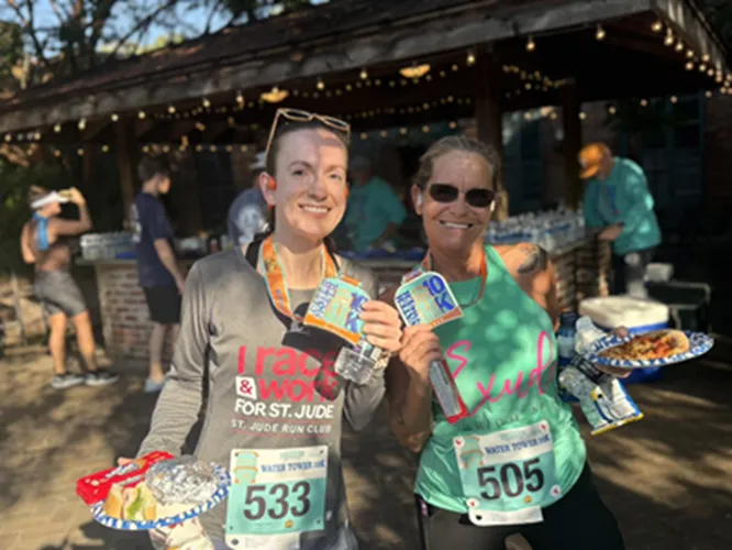 Two smiling female runners holding their race medals and plates of food after completing the Hernando Water Tower 10k and Half Marathon.