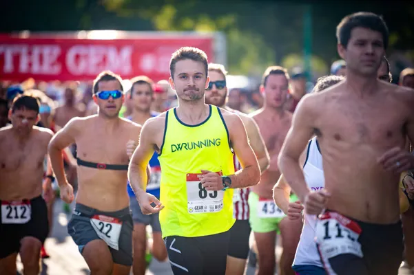 Runners in a race, with a focus on a man in a neon yellow tank top with the number 85.