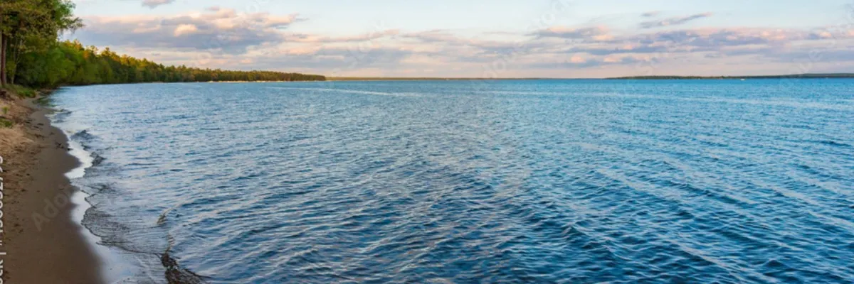 A wide shot of a calm lake with a tree-lined shore under a cloudy sky.