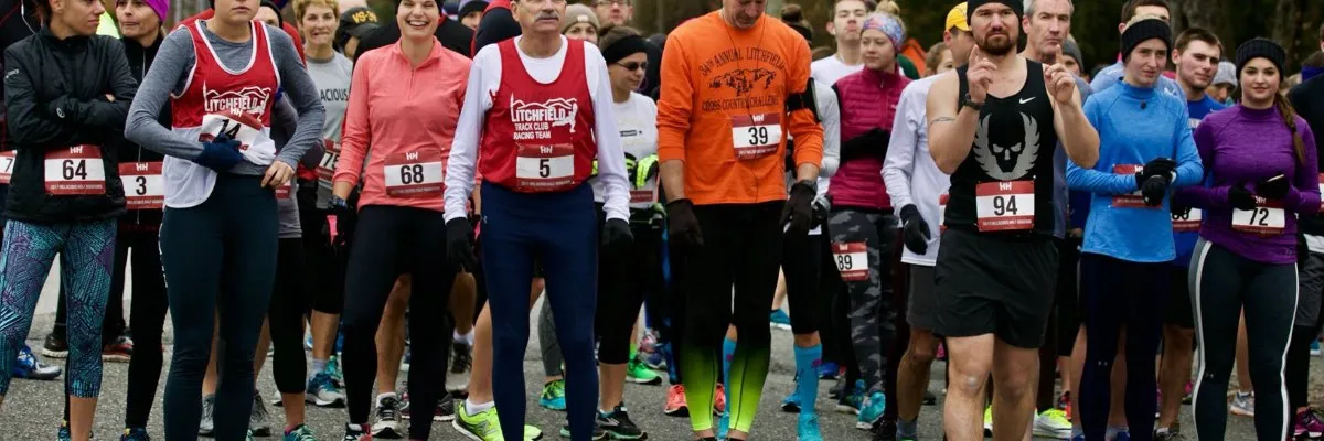 A group of runners in athletic wear, wearing bib numbers, stand at the start line of a race.