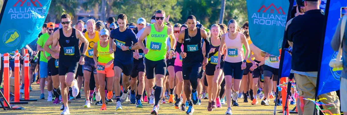 A large group of runners in a race, with bib numbers visible, starting the race.