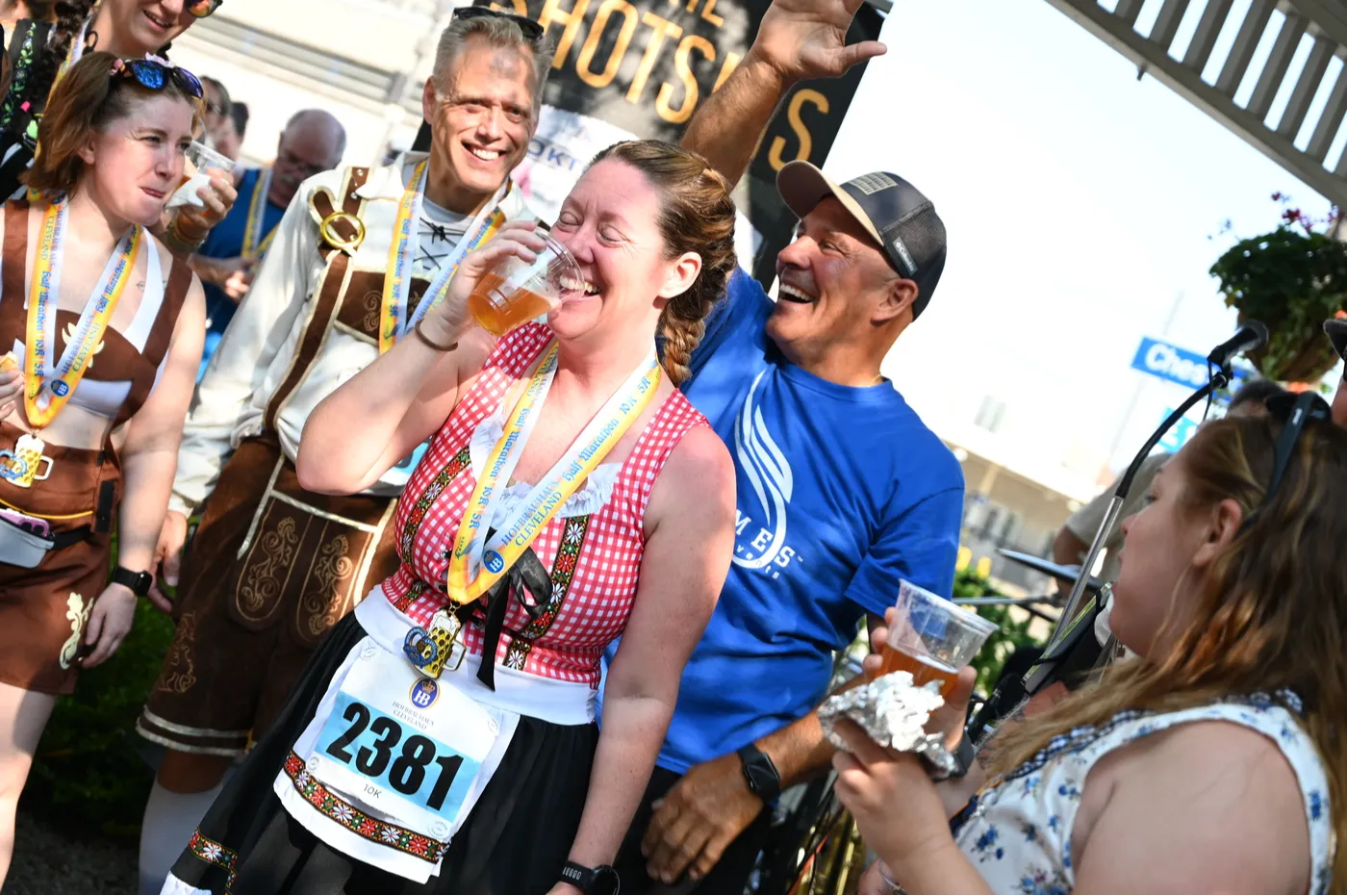 A group of people in festive attire, some wearing medals, laughing and holding drinks after a race.