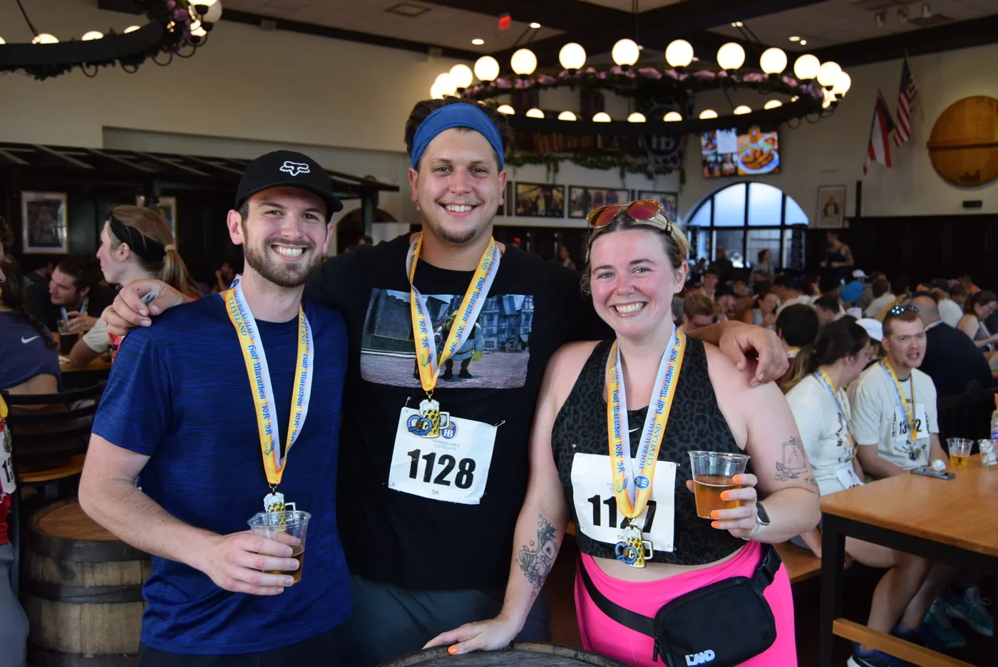 Three smiling runners, two men and one woman, wearing race medals and holding drinks, pose for a photo after completing a half marathon.
