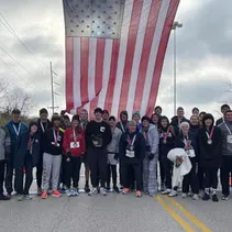 A group of runners, some wearing medals, stand together in front of a large American flag.