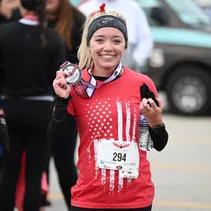 A smiling female runner wearing a red t-shirt with an American flag design and a race medal around her neck.