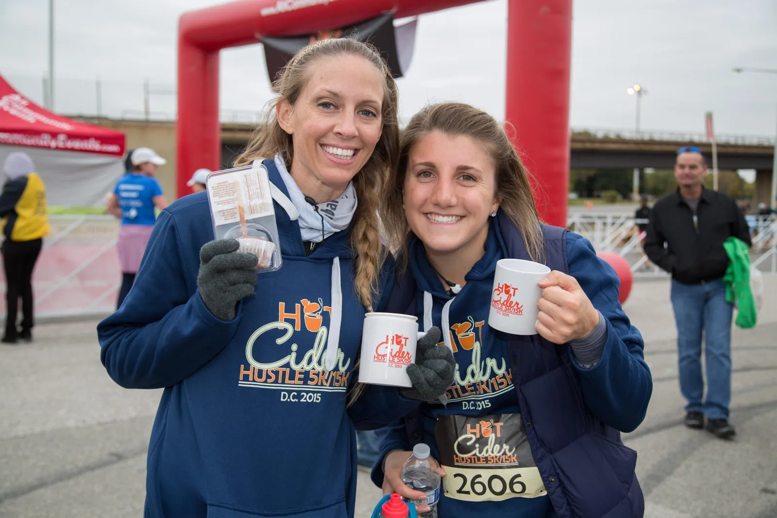 Two smiling women holding mugs and a cupcake at the Hot Cider Hustle race.