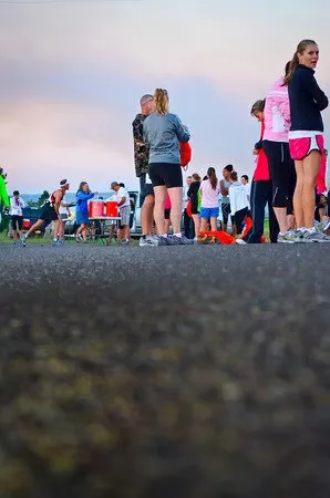 Runners gathered on a road before a race, with a cloudy sky in the background.