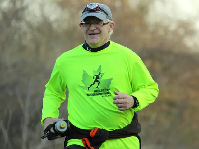 An older man with glasses and a headlamp runs while smiling, wearing a bright green long-sleeved shirt with a race logo.