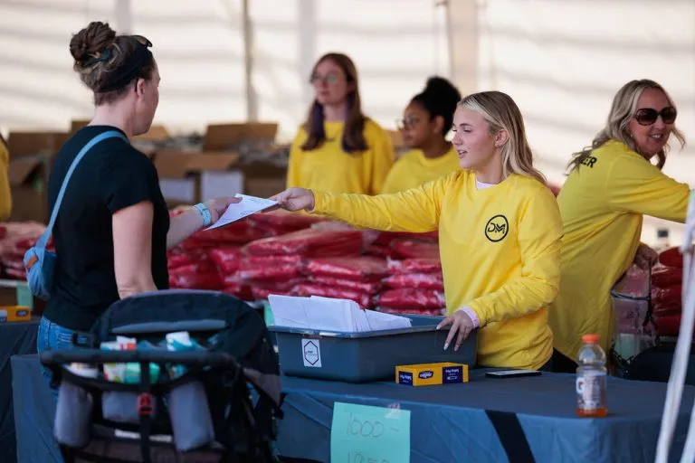 A volunteer in a yellow shirt hands a document to a participant at a race event.