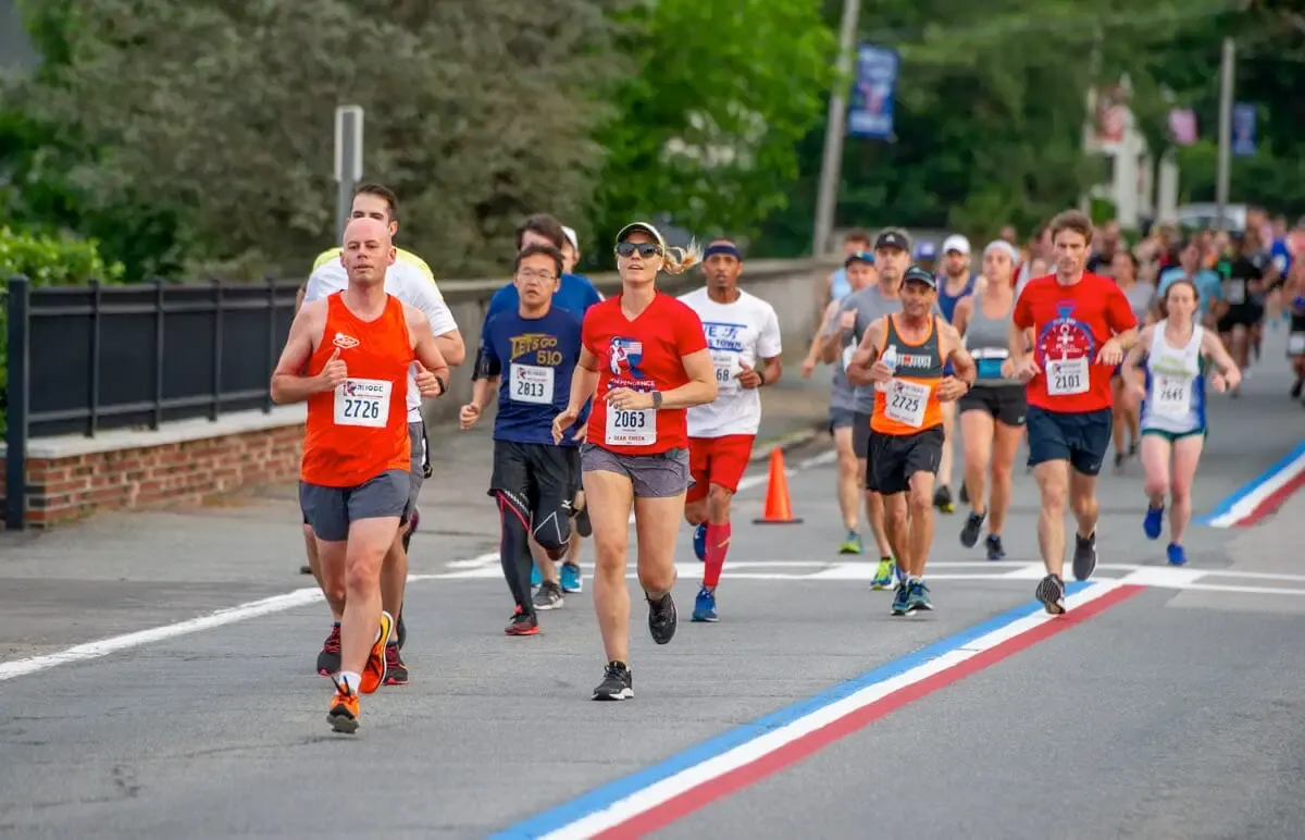 A group of runners in a race, with the lead runner in an orange singlet giving a thumbs up.