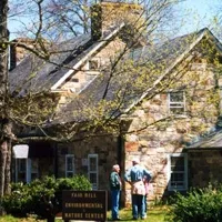 Two people stand near a stone building with a sign that reads 'Fair Hill Environmental Nature Center'.